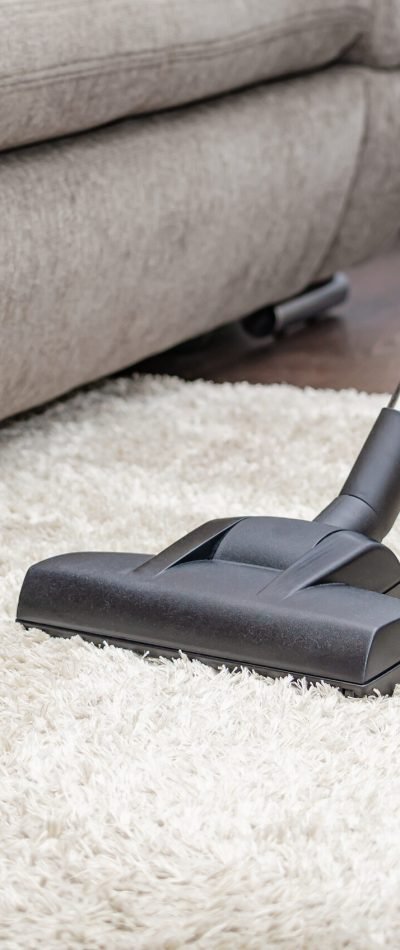 A woman vacuums a gray carpet with a vacuum cleaner. Cleaning and cleanliness concept.