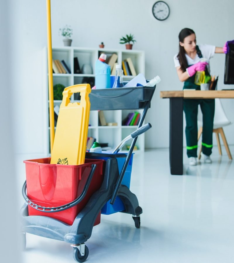young-female-janitor-cleaning-office-with-various-cleaning-equipment.jpg