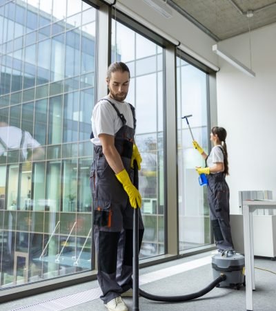 Vacuum cleaning. Young man in uniform vacuum cleaning the floor in the conference room